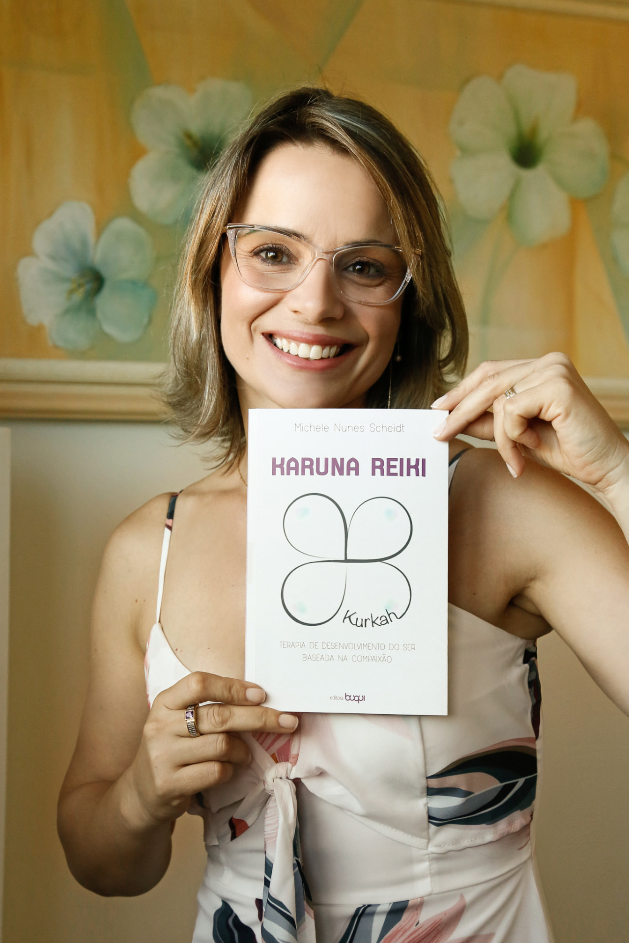 Michele segurando o livro Karuna Reiki à frente do corpo