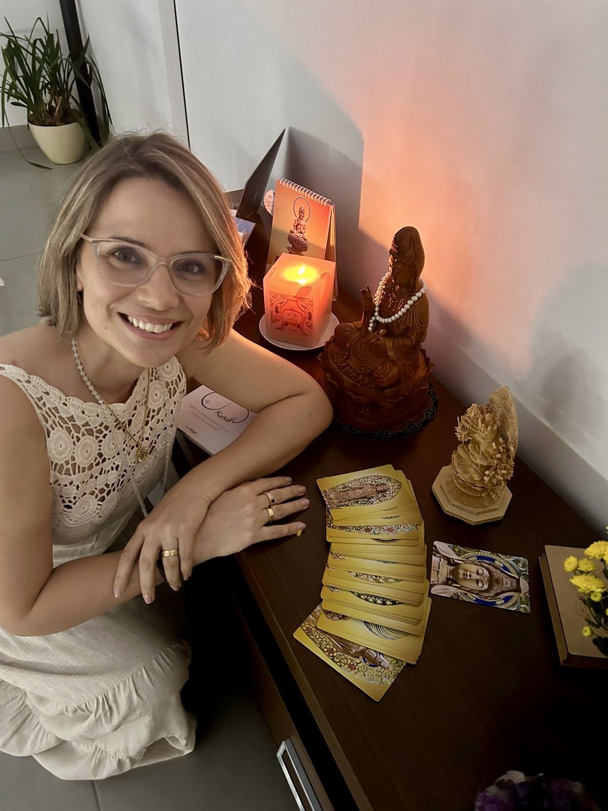 Michele diante de um altar com imagens de Kuan Yin, vela acesa e cartas do Oráculo abertas sobre a mesa
