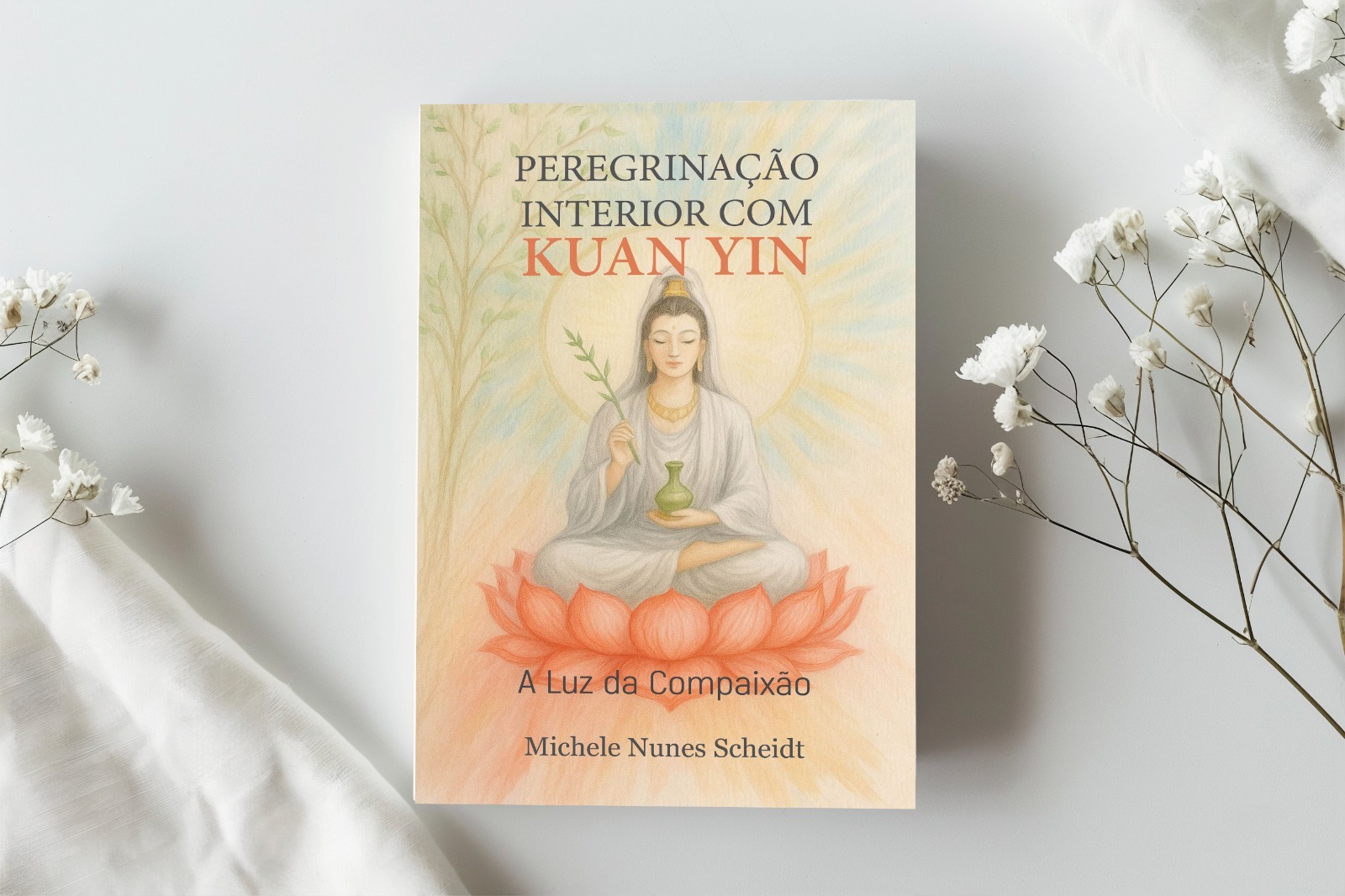 Livro Peregrinação Interior com Kuan Yin sobre tecido claro, ao lado de pequenas flores
